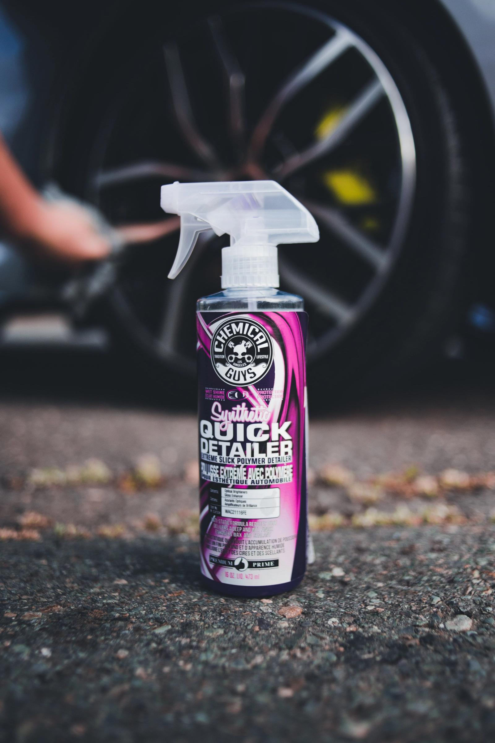 A car detailing spray bottle in focus with a car wheel blurred in the background