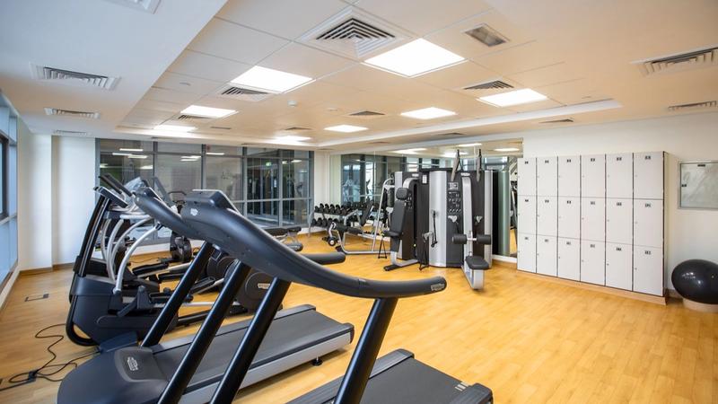 Bright gym interior with a row of treadmills, resistance machines and member lockers