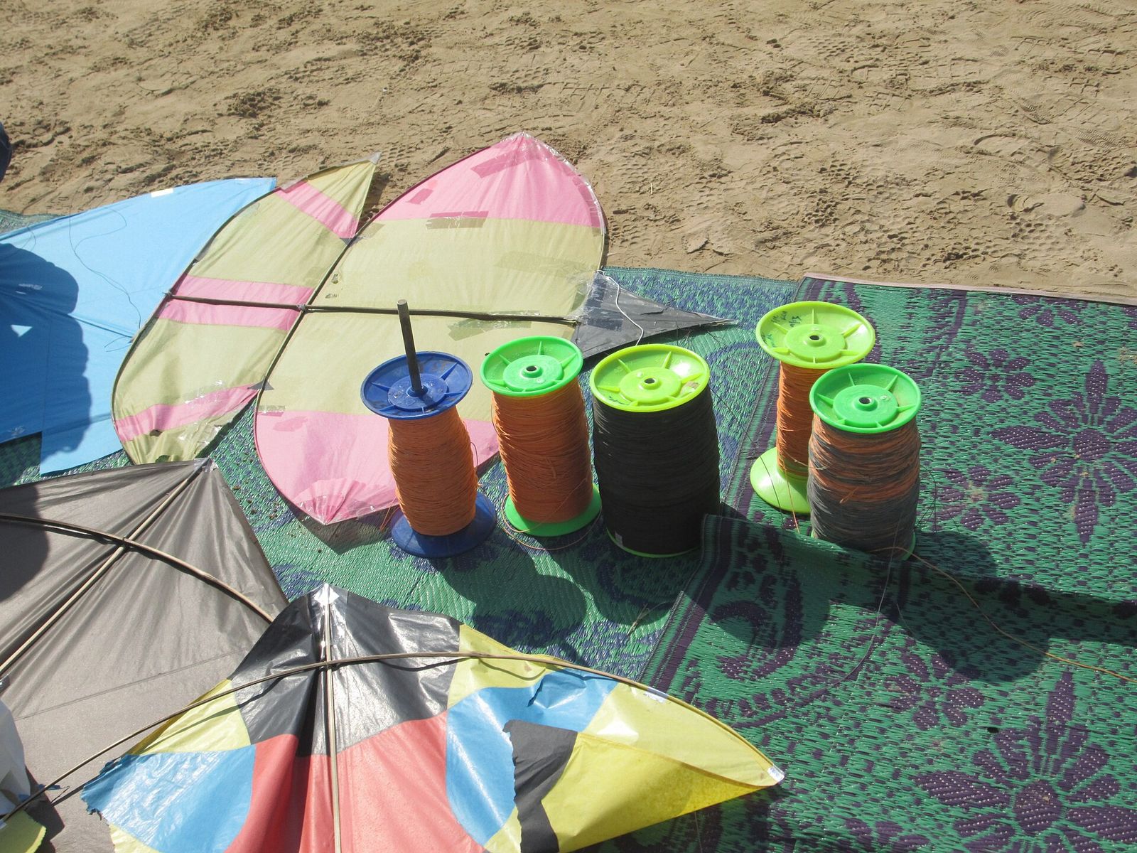 Traditional Pakistani style kites laid out beside spools of kite string wound on plastic pinnas