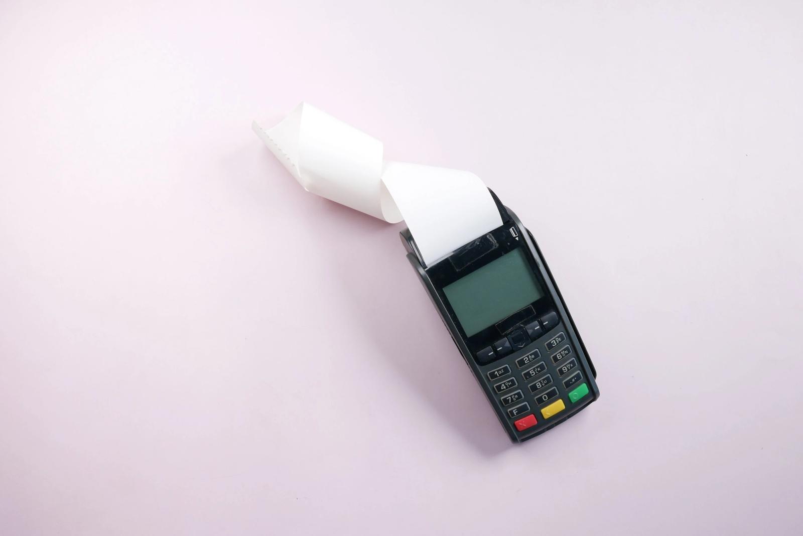 Card payment terminal with a printed receipt on a plain pink surface