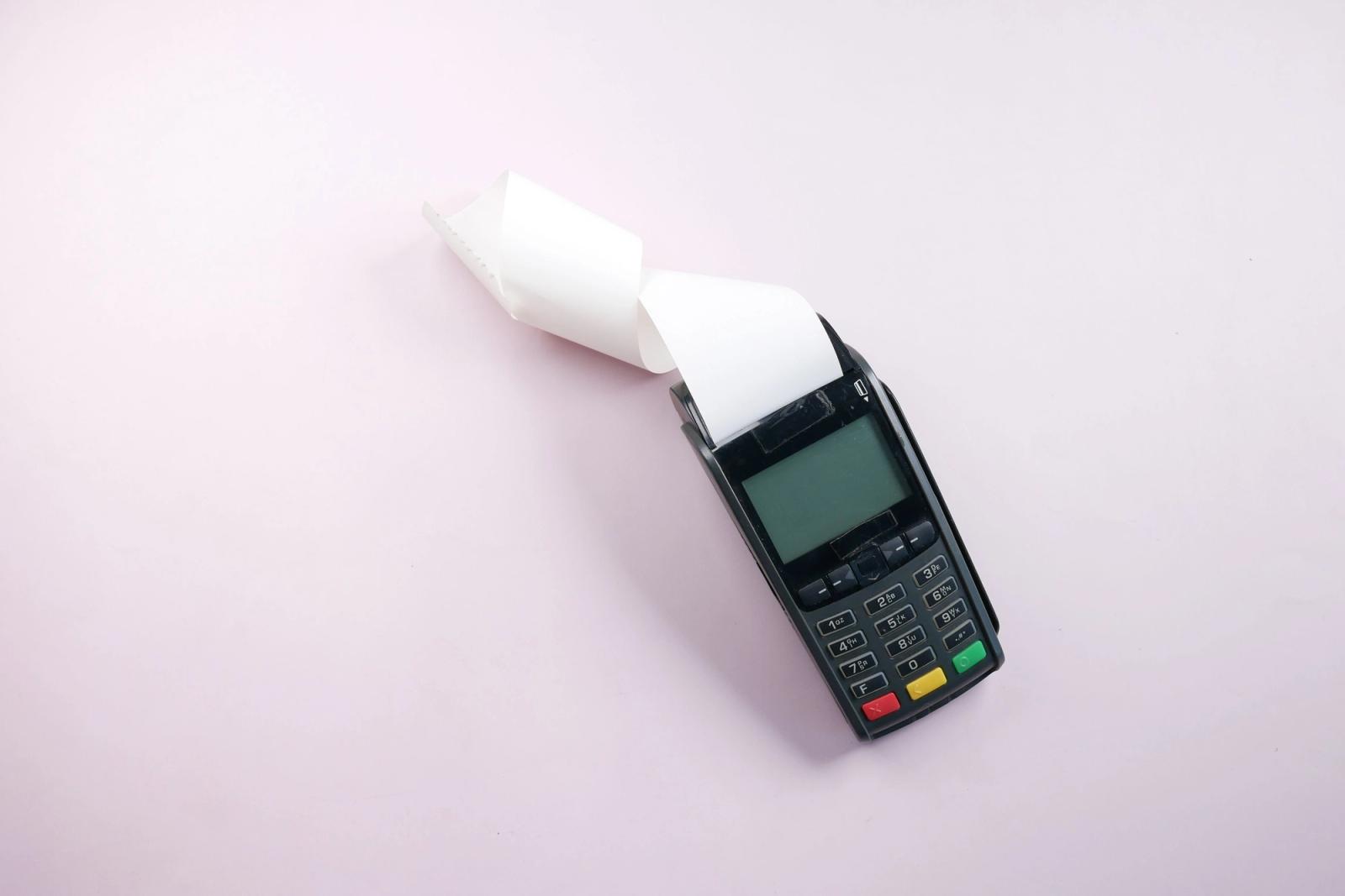 Card payment terminal with a printed receipt on a plain pink surface