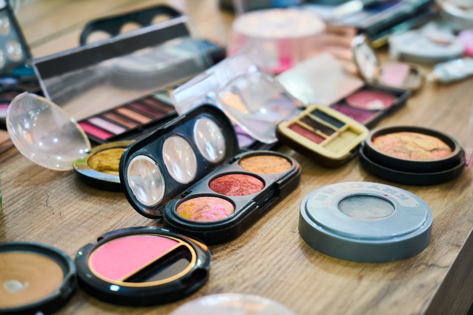 Makeup palettes, blush compacts and eyeshadow trays laid out on a wooden table