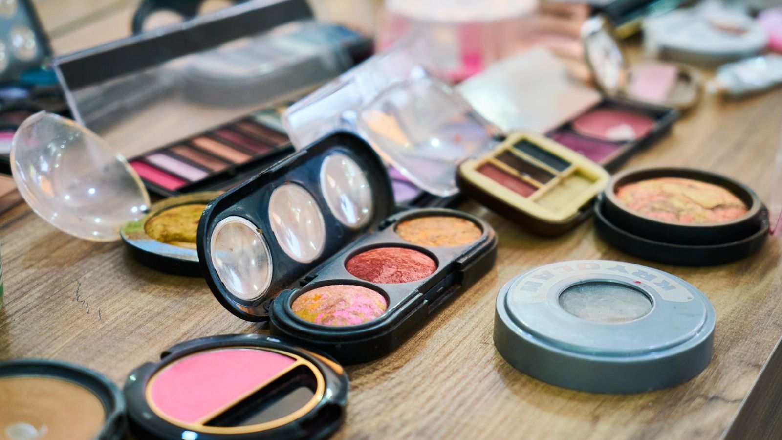 Makeup palettes, blush compacts and eyeshadow trays laid out on a wooden table