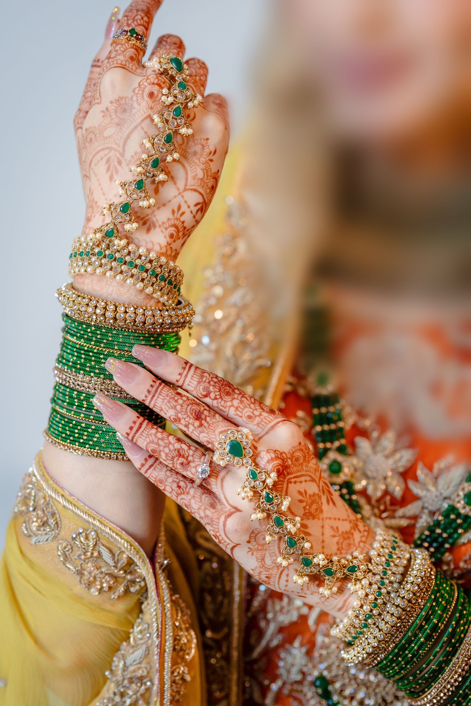 Close up of a bride's hands covered in mehndi, with gold rings and green glass bangles