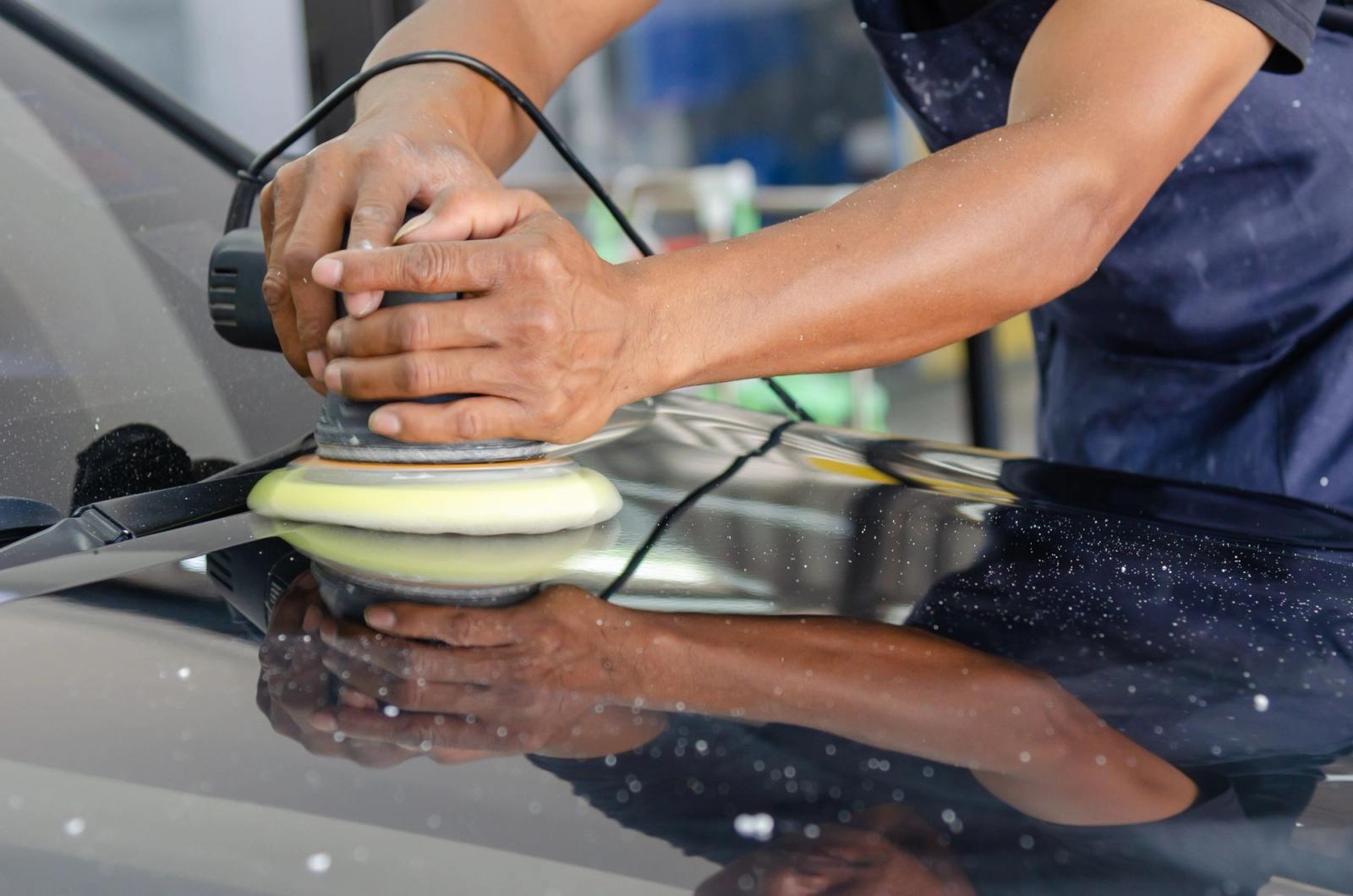Close-up of gloved hands using a machine polisher to buff the hood of a car during a detailing job