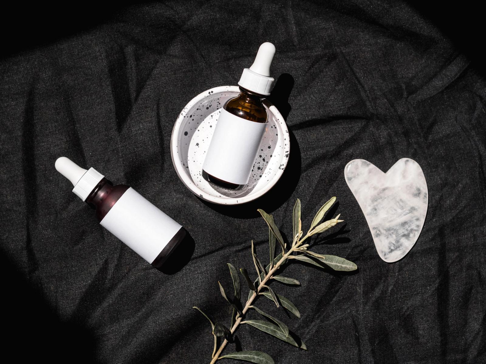 Skincare serum bottles and a gua sha tool arranged on a dark backdrop