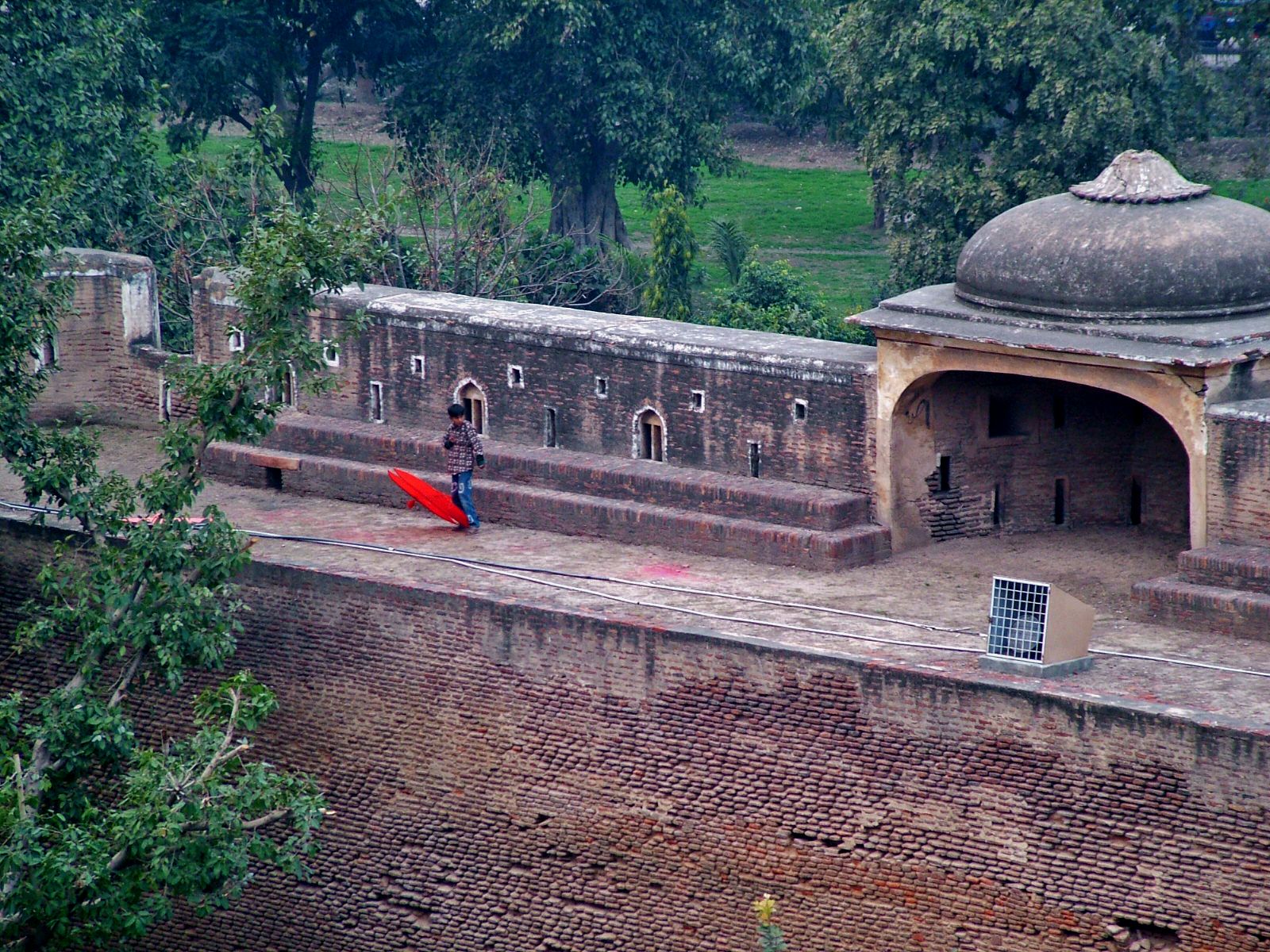 A child carrying a red kite along a brick terrace at Shahi Qila, the Lahore Fort