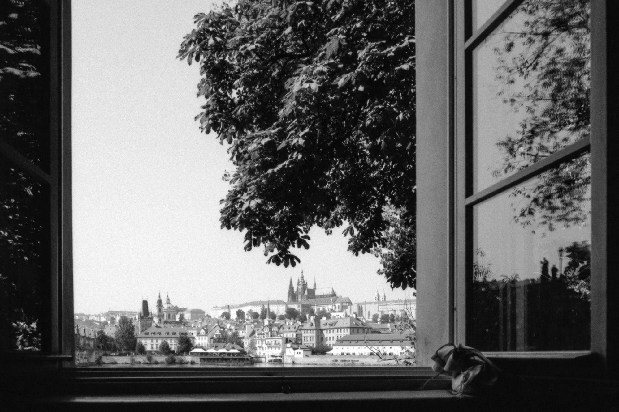 Durch ein offenes Fenster bietet sich ein atemberaubendes Panorama von Prag mit der Prager Burg und den historischen Dächern der Altstadt im Vordergrund.