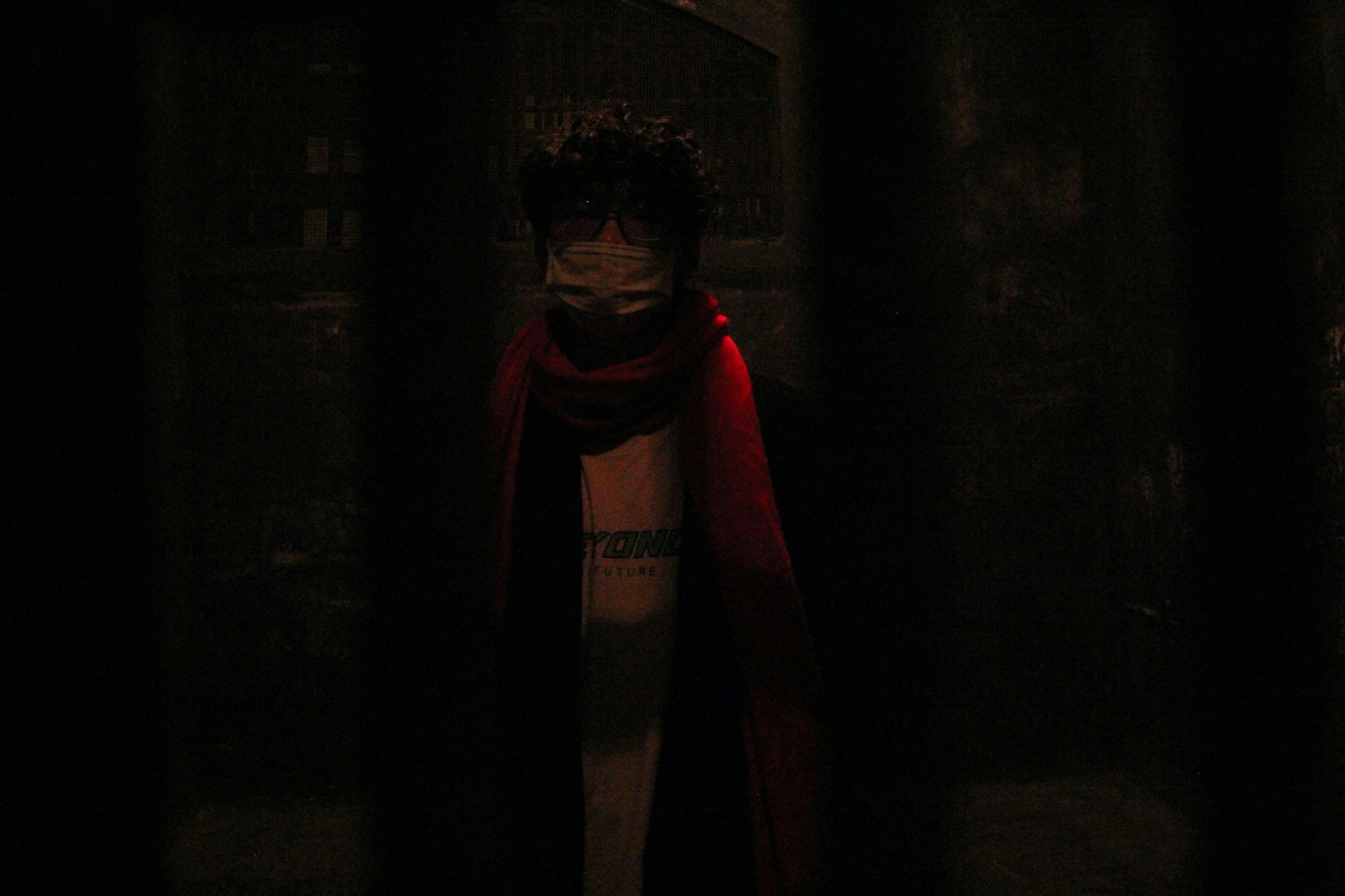 A figure stands in darkness behind bars.