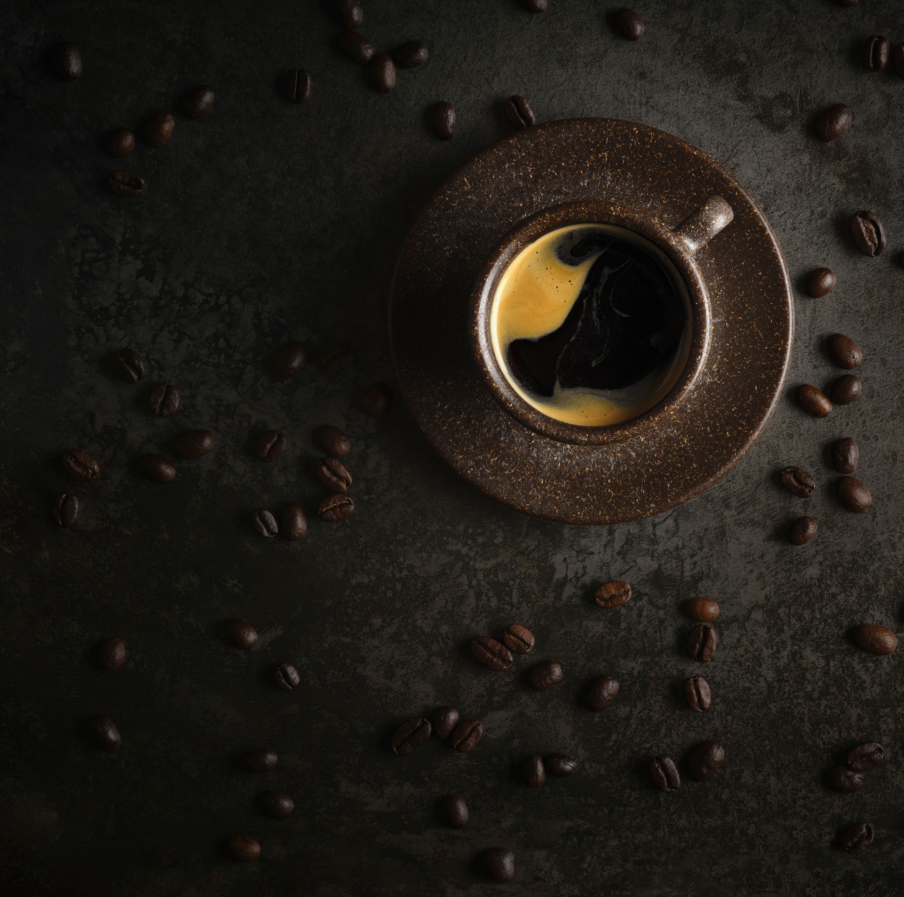 Overhead image of black coffee with whole beans in the background