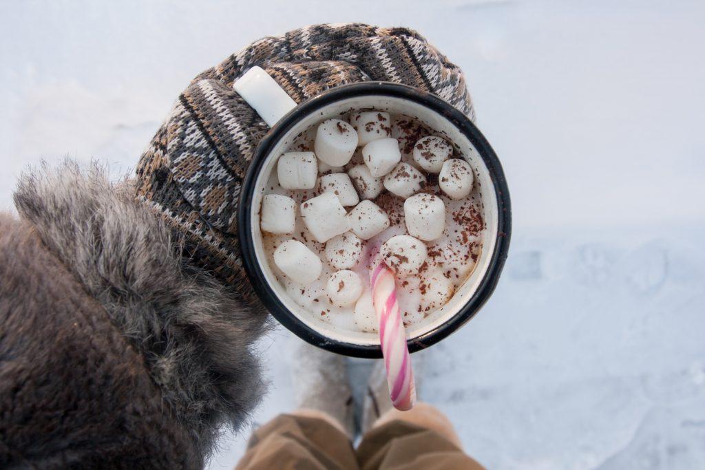 person wearing glove holding mug of hot chocolate with marshmallowss