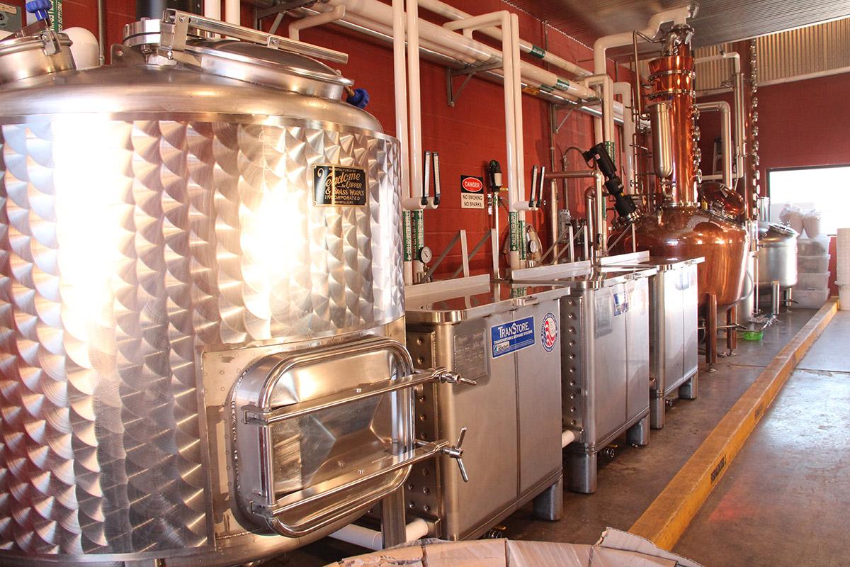 A photo of Moonshine University's still operation. From left to right there's a cooker, three fermenters, and a copper still