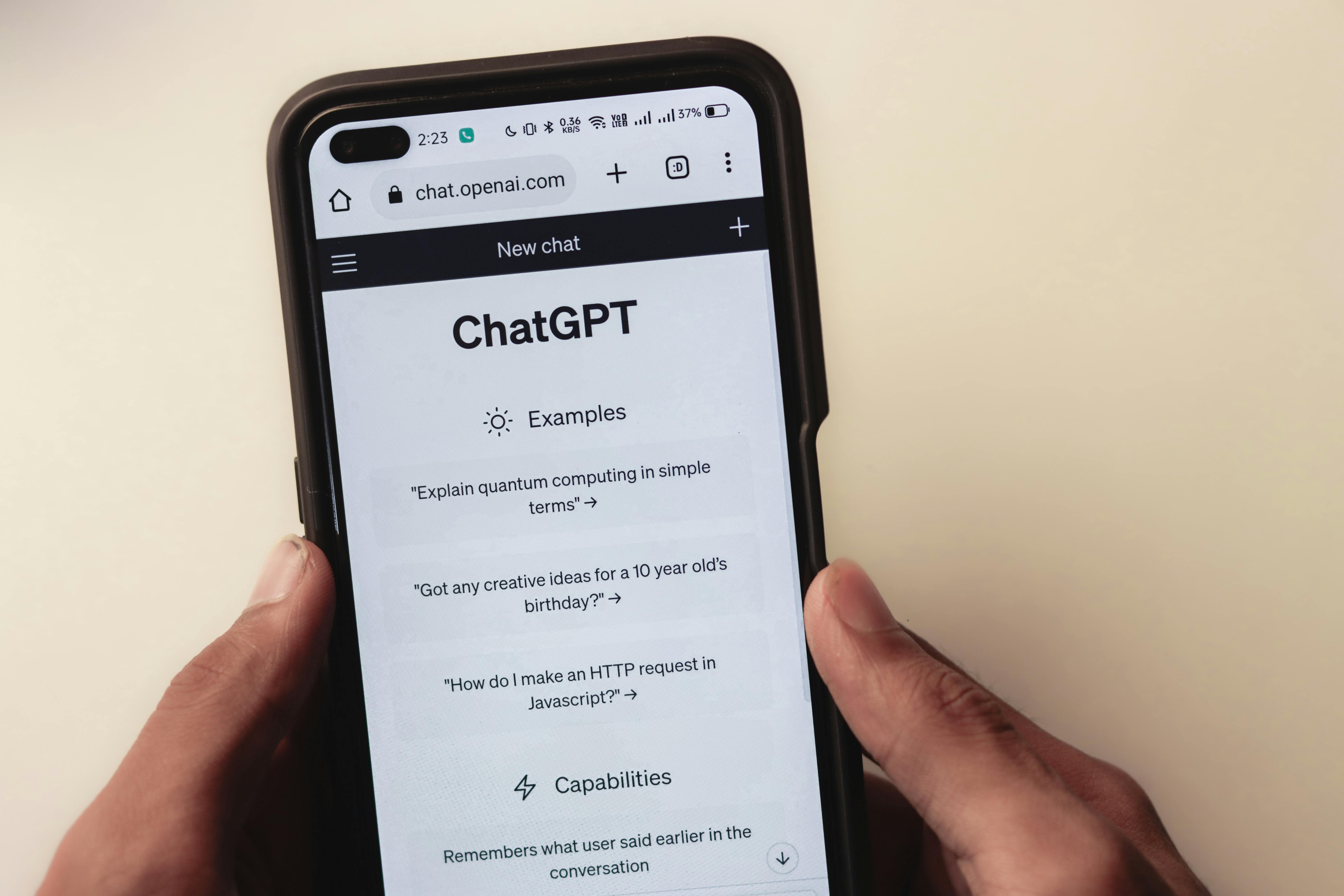 Hands holding a smartphone displaying the ChatGPT website with example prompts.