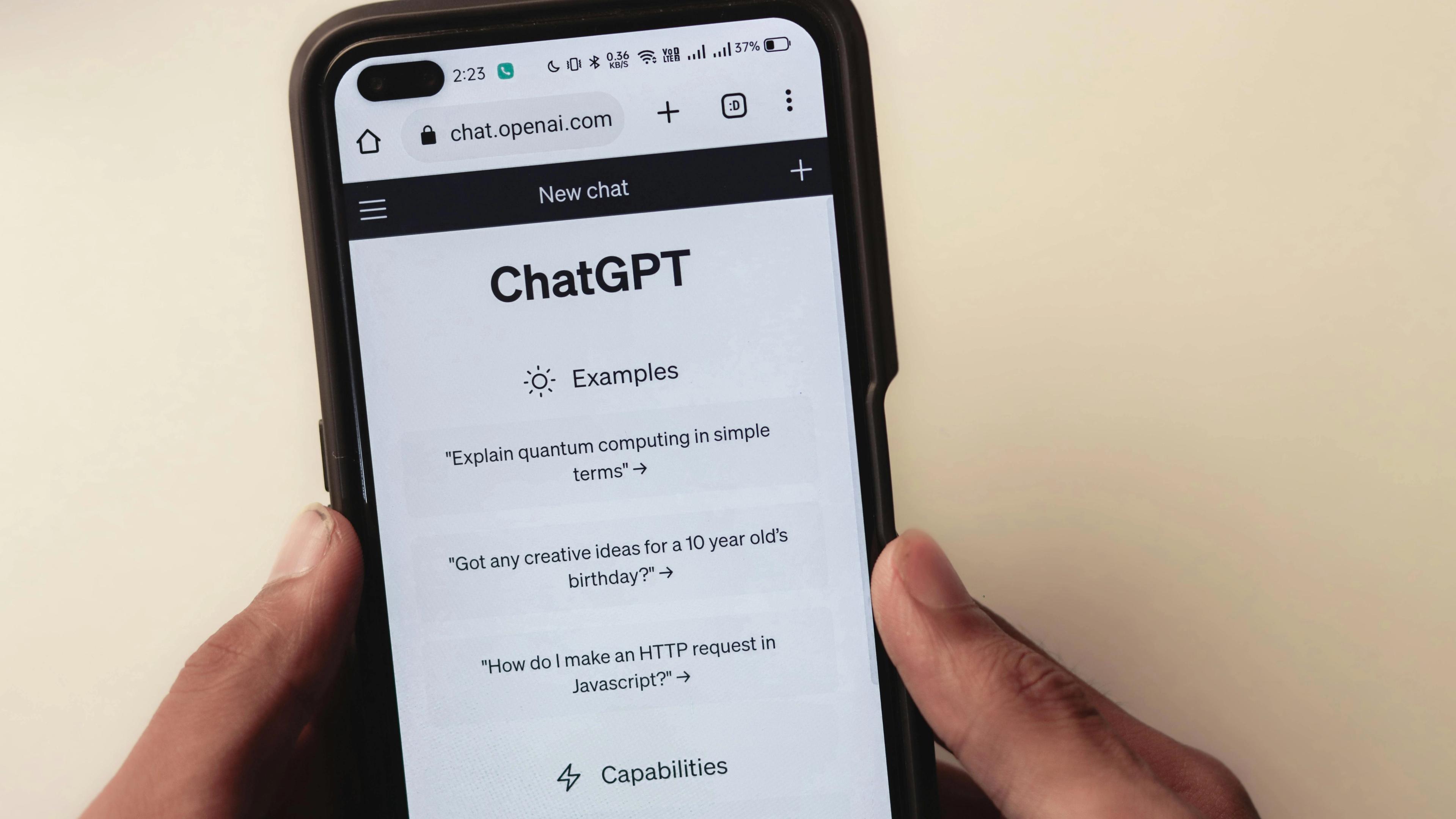 Hands holding a smartphone displaying the ChatGPT website with example prompts.