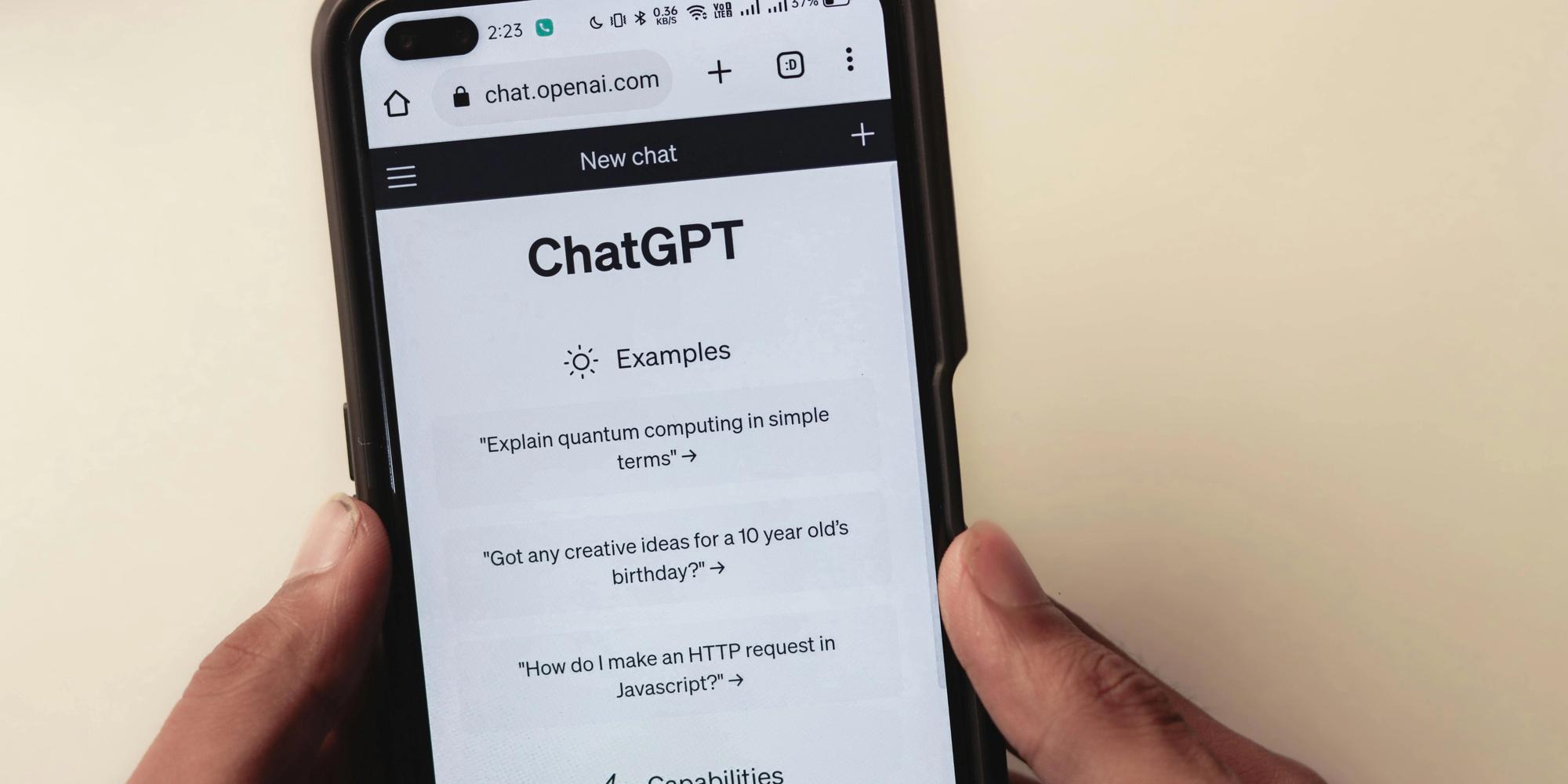 Hands holding a smartphone displaying the ChatGPT website with example prompts.
