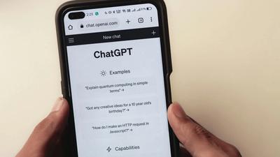 Hands holding a smartphone displaying the ChatGPT website with example prompts.