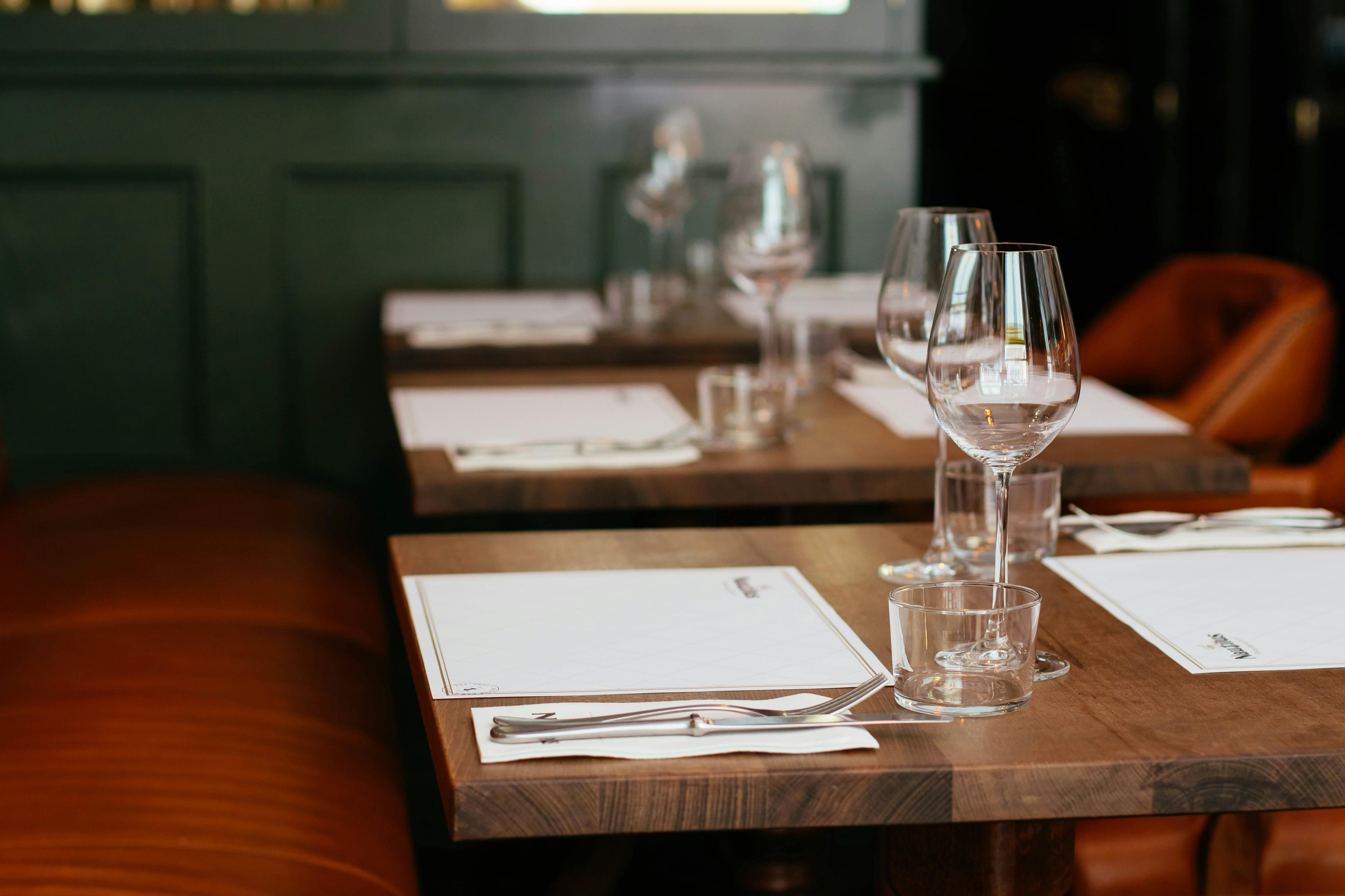 Set tables in a restaurant with wine glasses, cutlery, and leather booths.