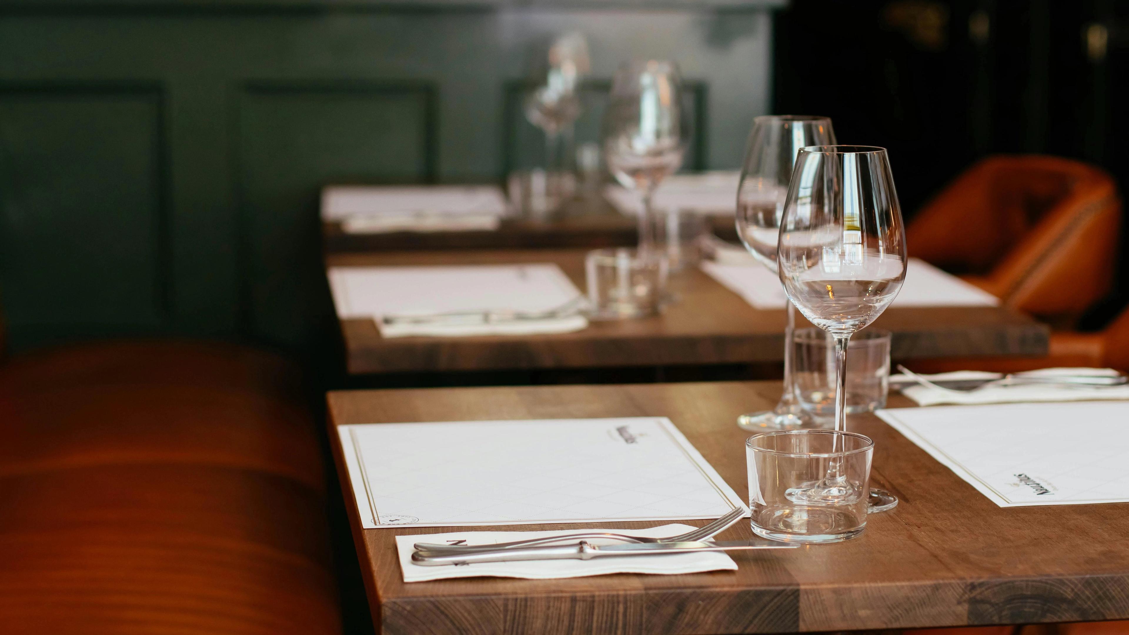 Set tables in a restaurant with wine glasses, cutlery, and leather booths.