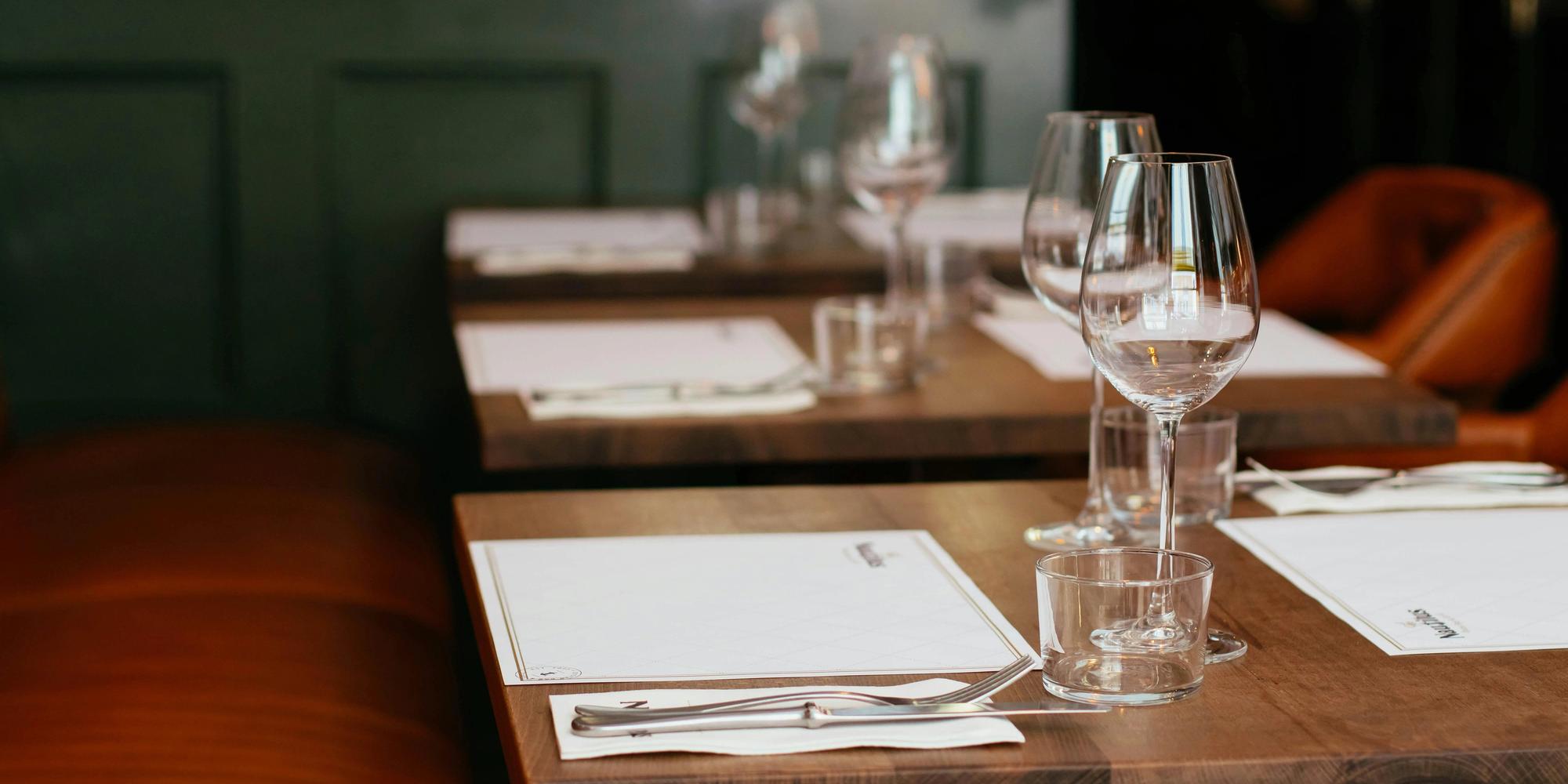 Set tables in a restaurant with wine glasses, cutlery, and leather booths.