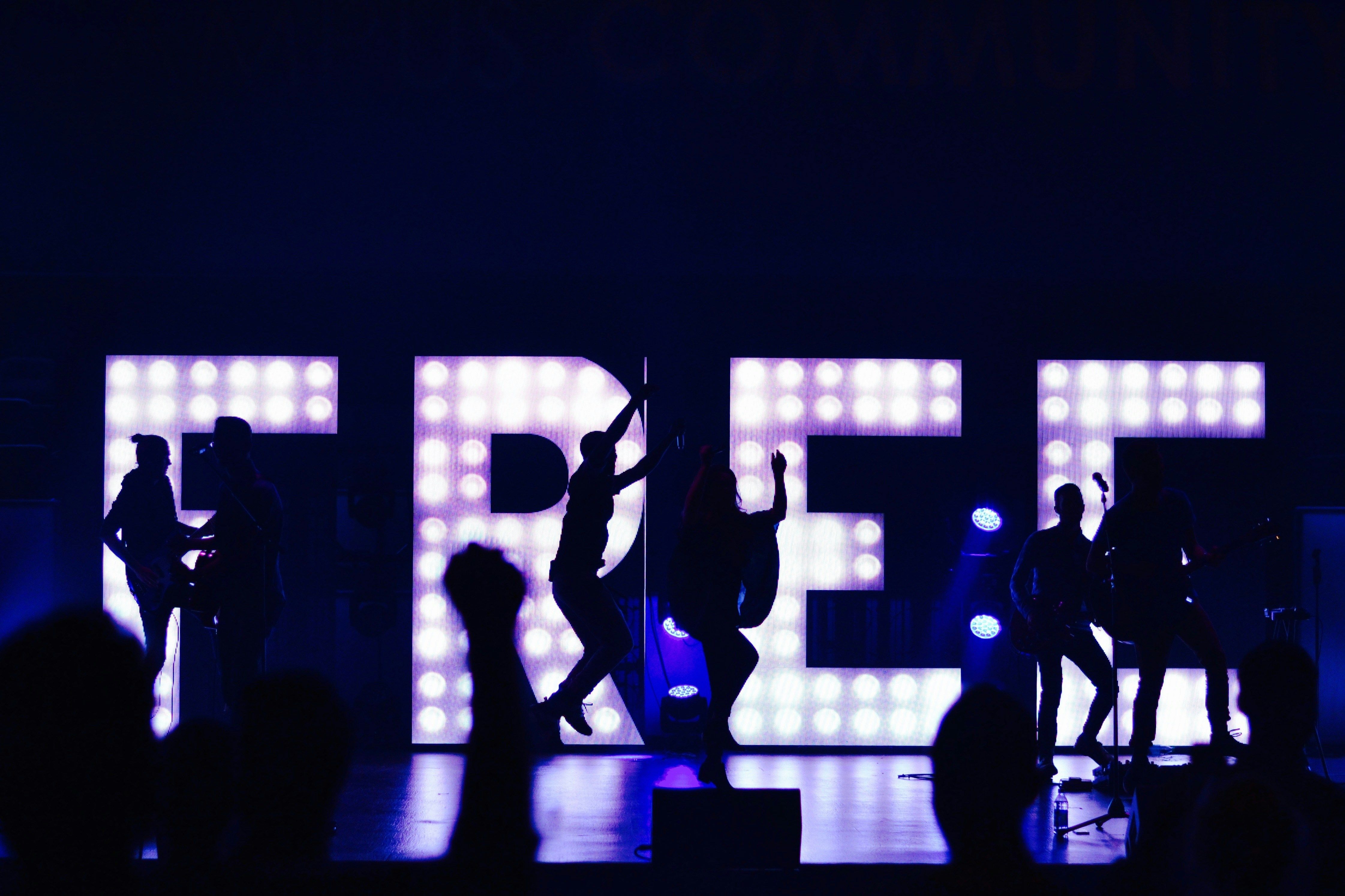 Concert with a band and dancers silhouetted against a glowing "FREE" sign.