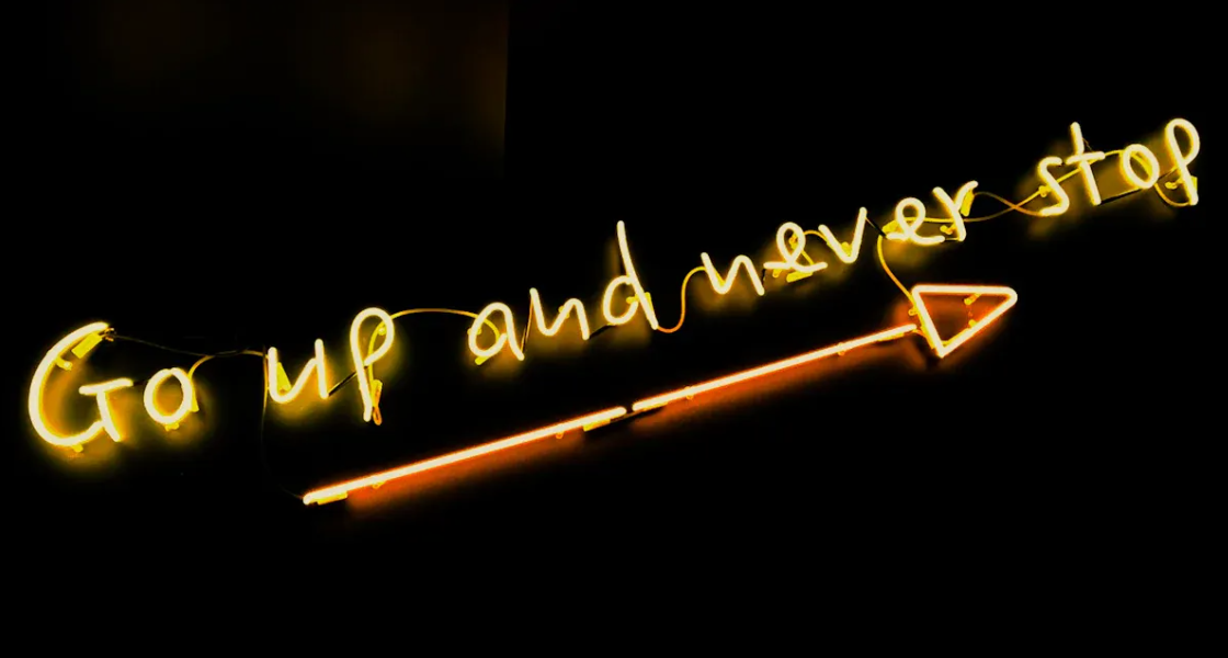 Yellow neon sign saying "Go up and never stop" with an arrow pointing right.