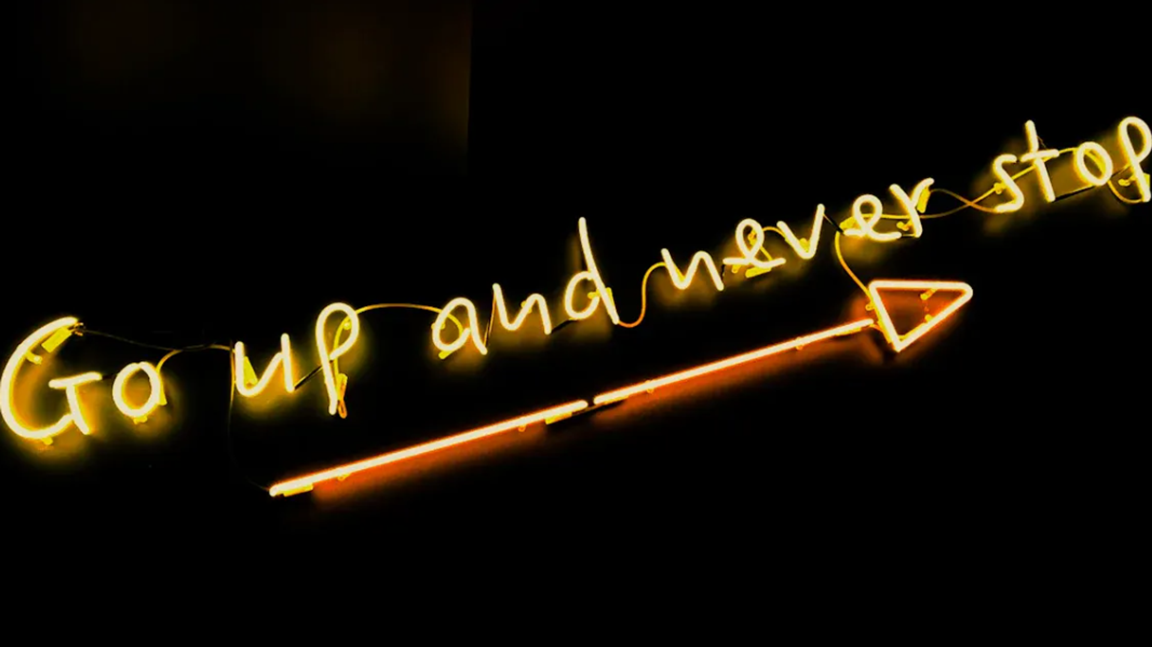 Yellow neon sign saying "Go up and never stop" with an arrow pointing right.