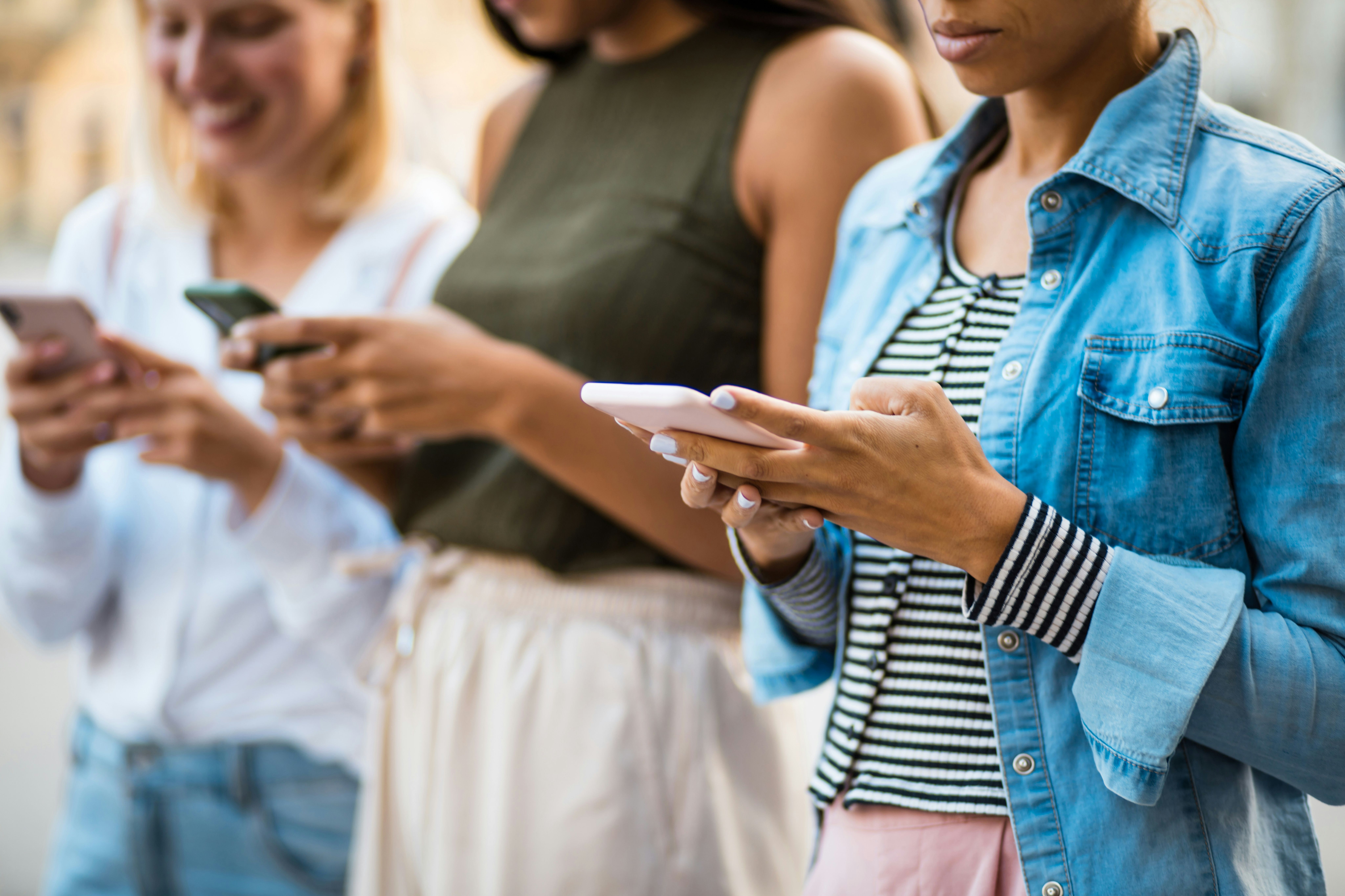 Three people standing outdoors, each looking down and using a smartphone.