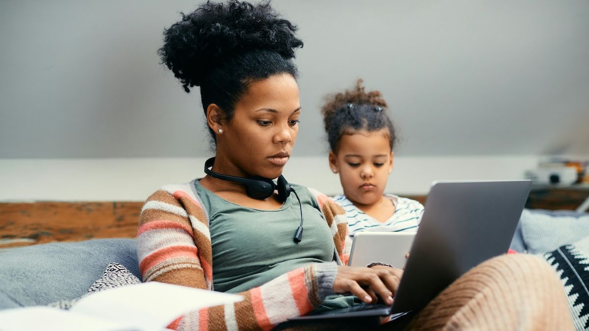 A female small business owner getting some work done on the couch at home with her daughter next to her