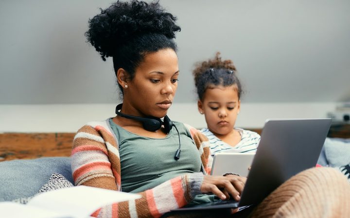 A female small business owner getting some work done on the couch at home with her daughter next to her