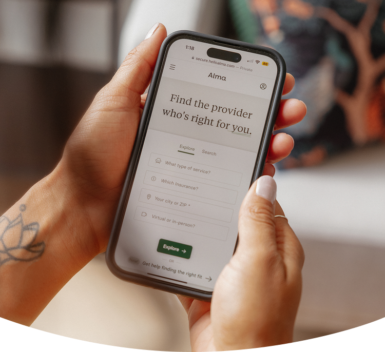 Person holding a smartphone with the Alma website open, showing a provider search tool to find the right therapist based on service, insurance, and location.