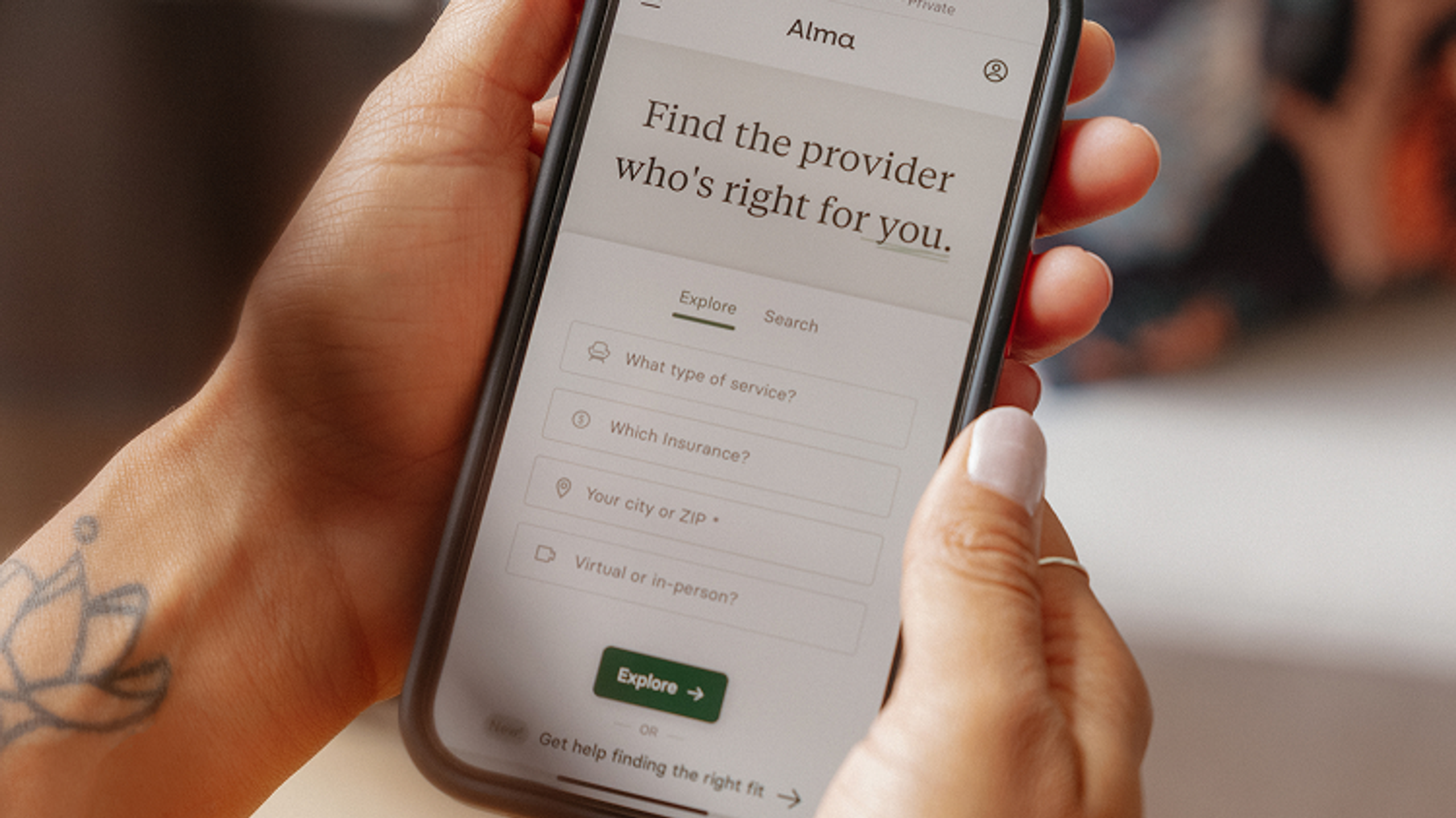 Person holding a smartphone with the Alma website open, showing a provider search tool to find the right therapist based on service, insurance, and location.