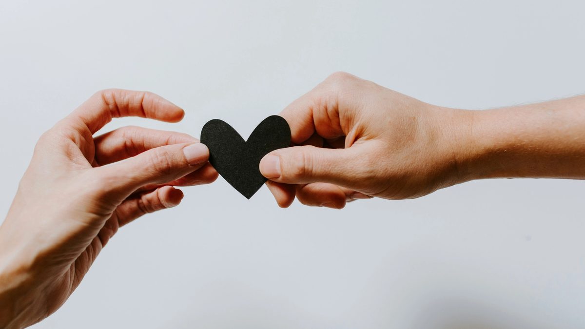 Two hands holding a black paper heart together.