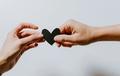 Two hands holding a black paper heart together.