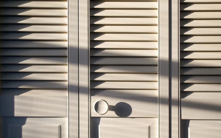 Closed closet doors thrown into relief by shadows from bright afternoon sunlight.