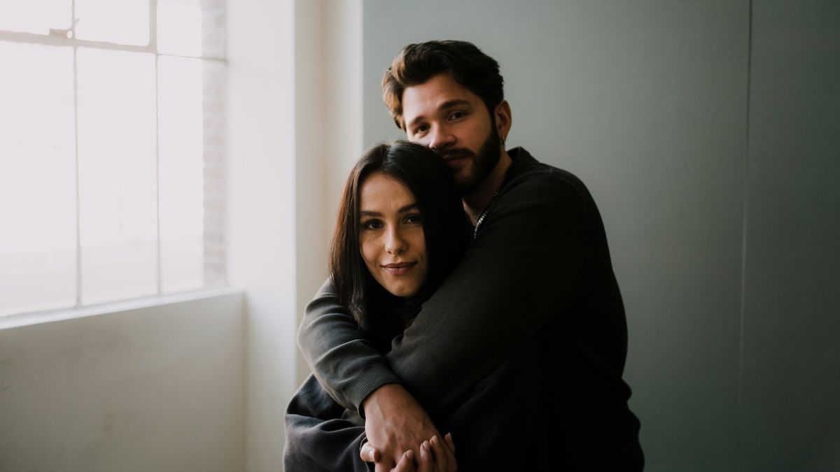 A man standing behind a woman with his arms wrapped around her shoulders
