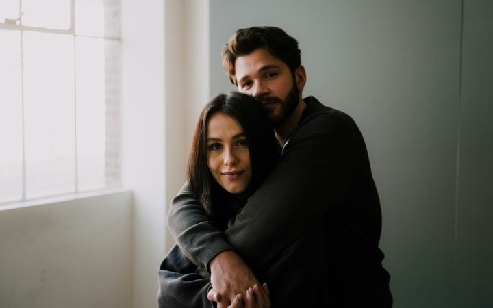A man standing behind a woman with his arms wrapped around her shoulders