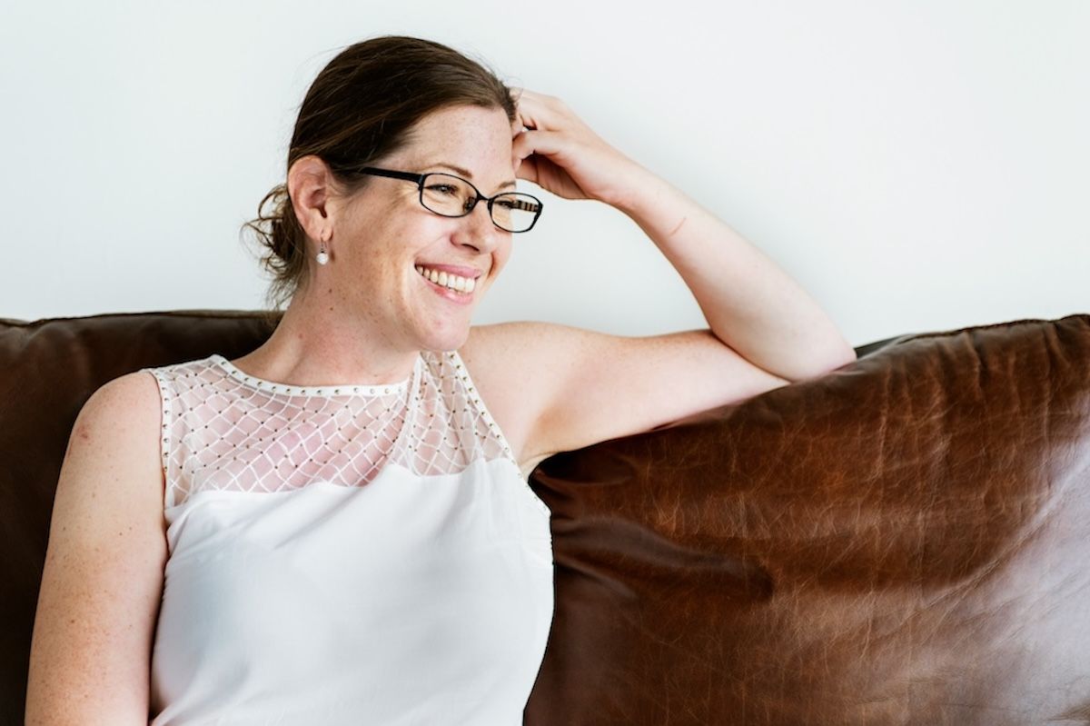 a female therapist wearing glasses sits on a couch smiling