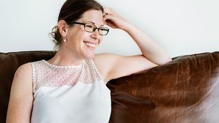 a female therapist wearing glasses sits on a couch smiling