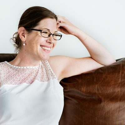 a female therapist wearing glasses sits on a couch smiling
