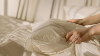 An image of two hands gently placing a pillow in white linens on a sun drenched bed.