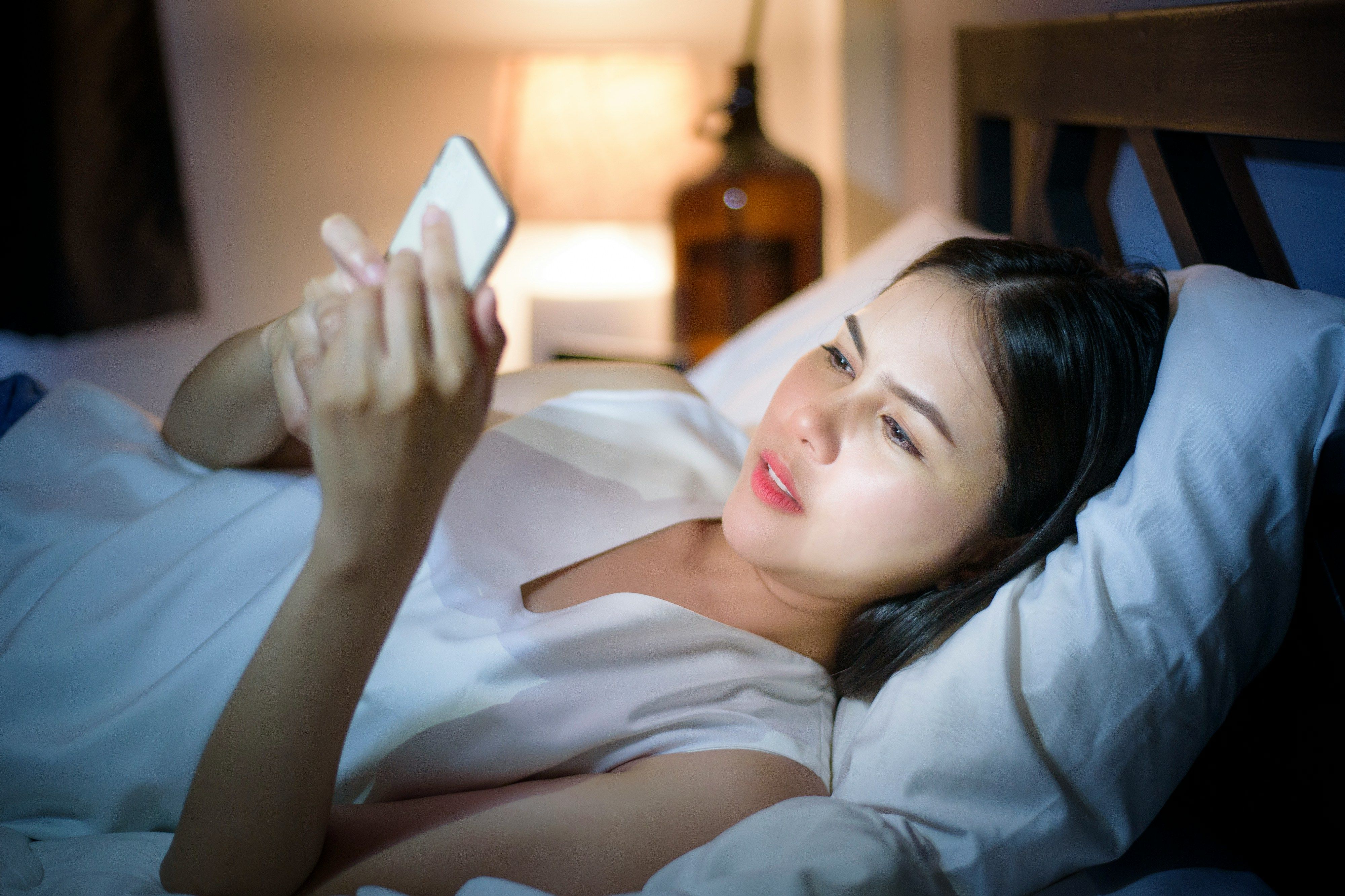Woman lying in bed at night looking at her smartphone screen