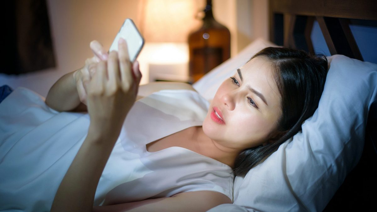 Woman lying in bed at night looking at her smartphone screen
