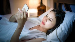 Woman lying in bed at night looking at her smartphone screen