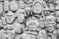 Dozens of cartoonish, crowded faces carved in relief on a grey concrete wall.