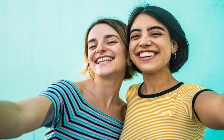 Two women friends wearing t-shirts smiling in front of a blue wall.