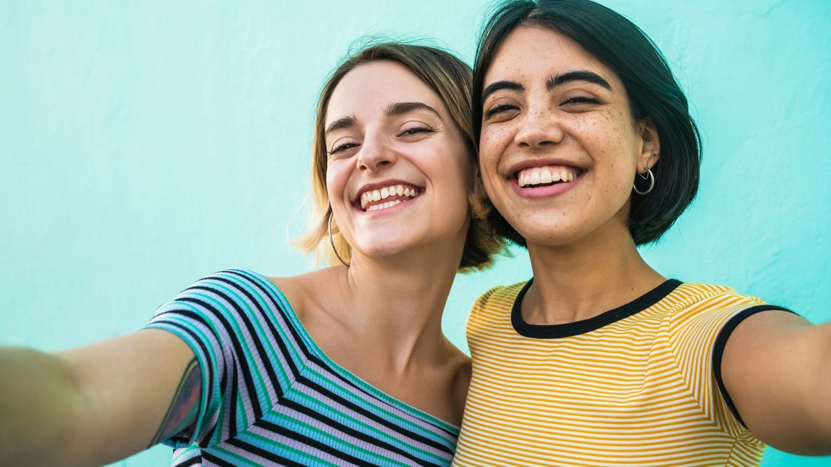 Two women friends wearing t-shirts smiling in front of a blue wall.