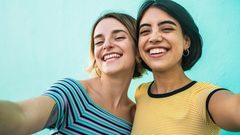 Two women friends wearing t-shirts smiling in front of a blue wall.