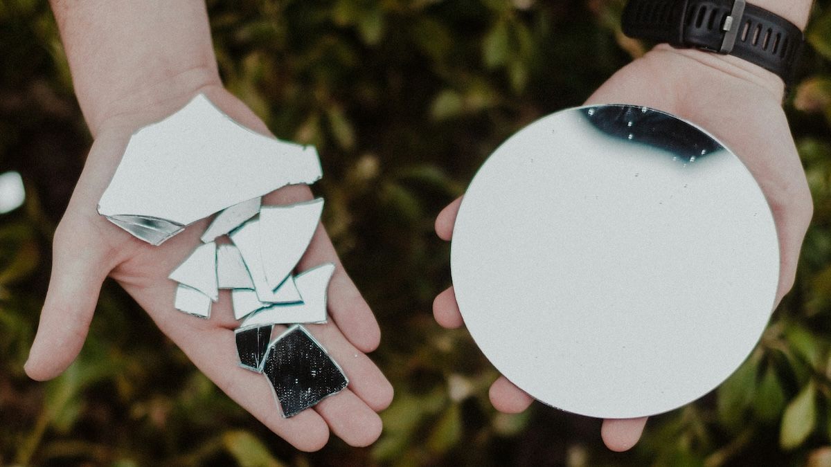 a person holding parts of a broken mirror in one palm and a whole, unbroken mirror in their other palm