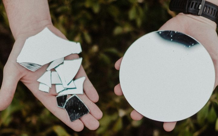 a person holding parts of a broken mirror in one palm and a whole, unbroken mirror in their other palm