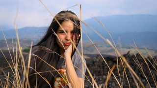 Woman in orange and white floral dress standing on brown grass field during daytime